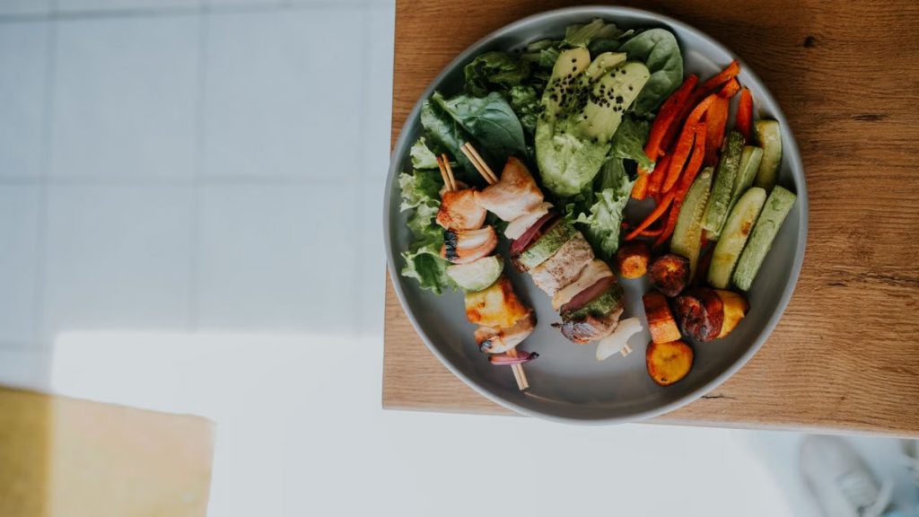 Top view of a vibrant platter with grilled skewers and fresh vegetables on a wooden table.